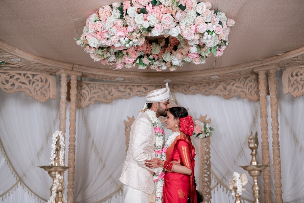 Photo Elegant wedding couple using vintage-style photo booth, floral garland backdrop, guests laughing, soft romantic lighting.