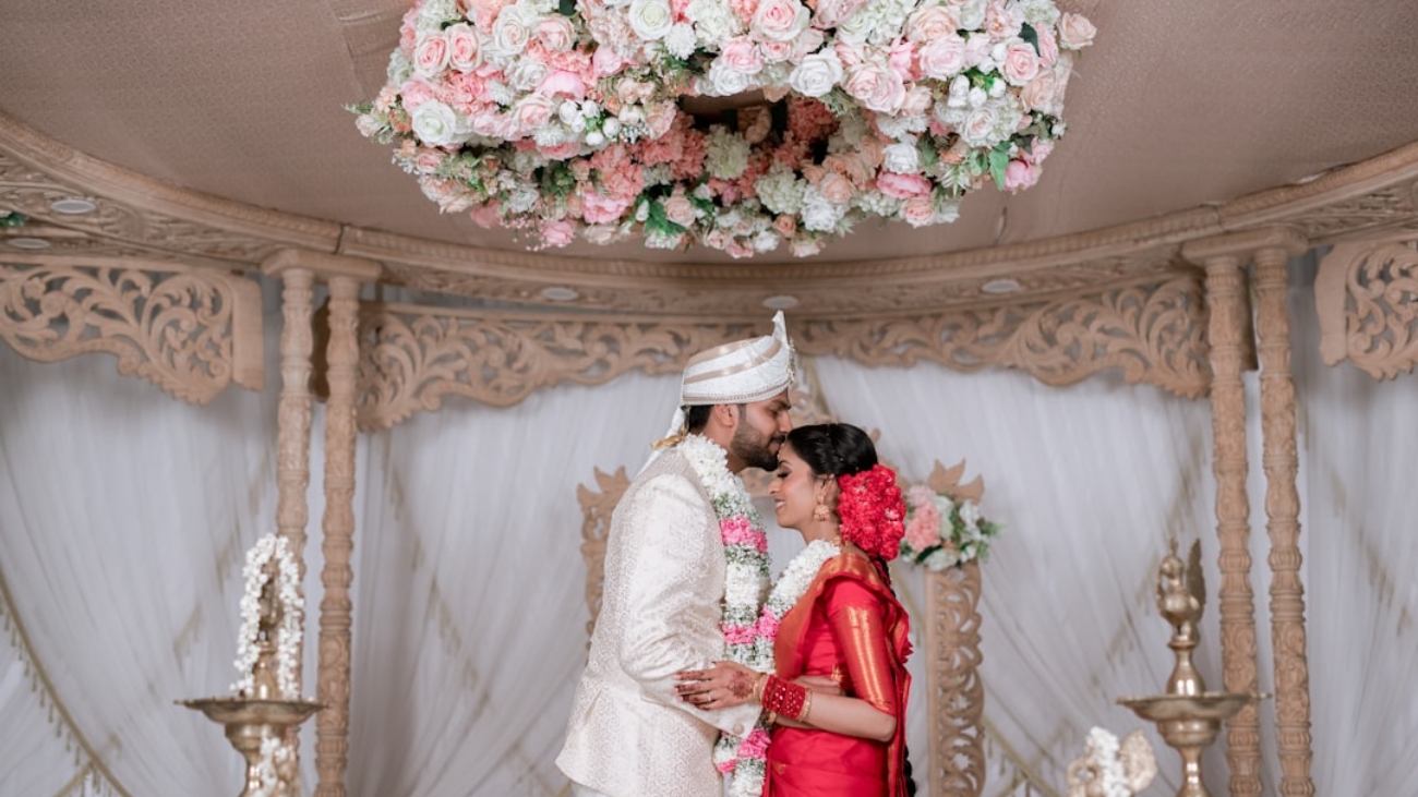 Photo Elegant wedding couple using vintage-style photo booth, floral garland backdrop, guests laughing, soft romantic lighting.