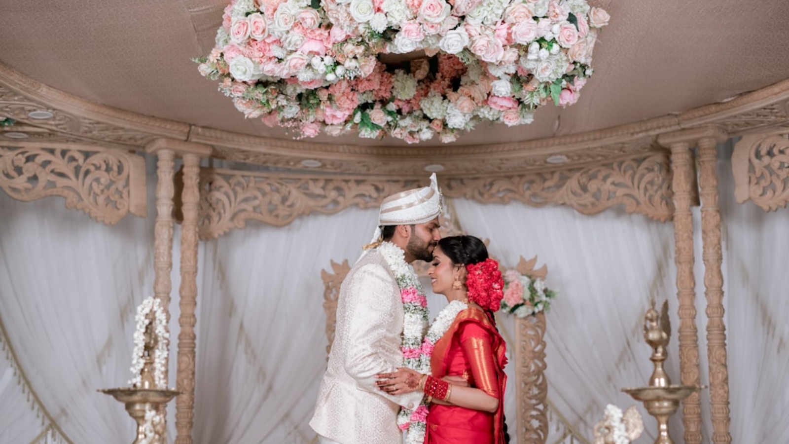 Photo Elegant wedding couple using vintage-style photo booth, floral garland backdrop, guests laughing, soft romantic lighting.
